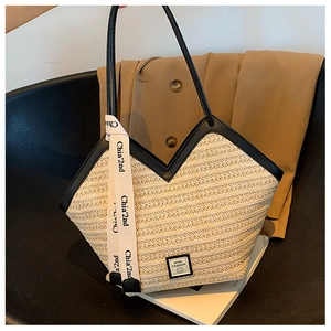 Detail of woven straw tote bag with black leather handles and decorative ribbon accent
