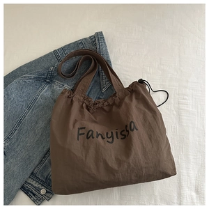 Brown nylon tote bag detail with ruffled opening and black drawstring closure on denim