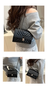 Detail of a black chevron quilted crossbody bag with silver chain and metal clasp
