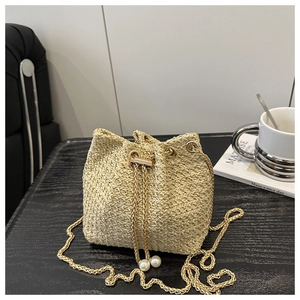 Close-up of woven straw bucket bag with gold chain strap and pearl drawstring details