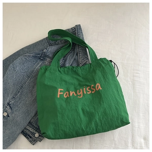 Macro detail of green canvas tote bag with orange lettering and drawstring texture