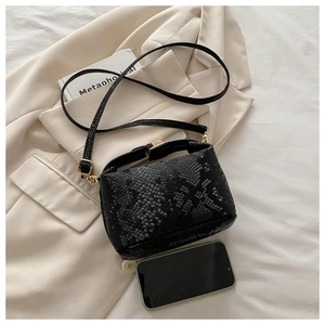 Close-up of black snake pattern texture on crossbody bag with gold hardware and phone reference