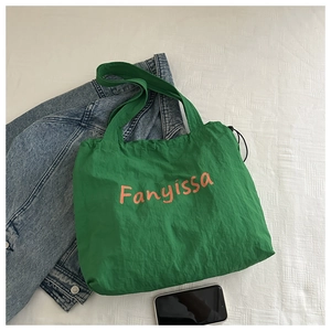 Flat lay of a green canvas tote bag with orange lettering next to a denim jacket and phone