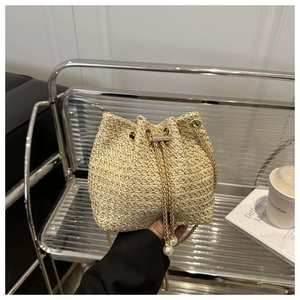 Close-up of beige woven bucket bag featuring elegant pearl charms and gold chain strap