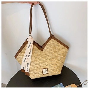 Detail of hand-woven straw tote with V-shaped opening and brown leather handles