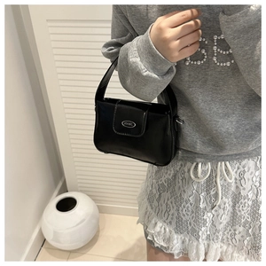 Détail du sac à main noir en cuir synthétique brillant porté à l'épaule