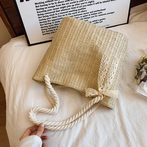 Beige straw tote bag with white rope handles and lace bow detail for summer beach travel