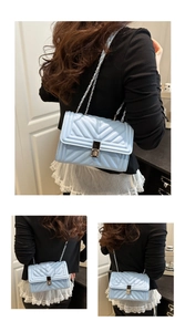 Detail view of light blue quilted crossbody bag with silver rotating lock and chain strap