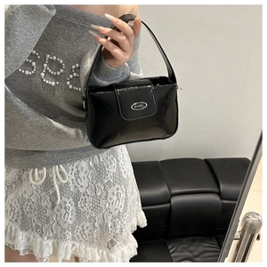 Close-up of black patent leather shoulder bag with a silver oval metal JWHW logo plate