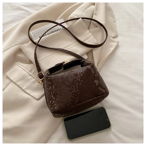 Detail of dark brown snakeskin embossed bucket bag with gold hardware and shoulder strap