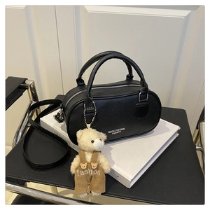 Close-up of black litchi grain bowling bag with cute plush bear charm on white books