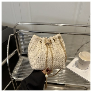 Detail of cream woven bucket bag with elegant gold chain strap and pearl charm accent