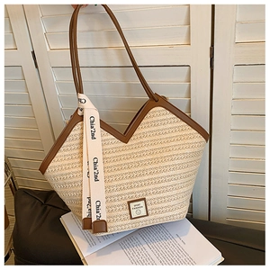 Detail of woven straw tote bag with brown leather trim and decorative ribbon strap