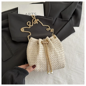 Close-up of beige woven bucket bag with gold chain strap and elegant pearl accents