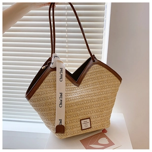 Detail of woven straw tote bag featuring brown faux leather trim and white ribbon charm