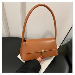 Détail d'un sac sous le bras en similicuir caramel avec un fermoir en métal doré chic