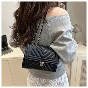 Detail of a black quilted leather crossbody bag with silver chain strap and metal lock