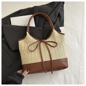Detail of handwoven straw tote bag with brown leather trim and delicate bow accent
