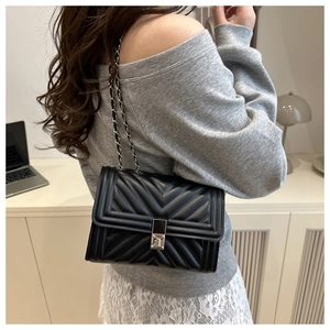 Detailed view of black quilted crossbody bag with metal chain strap and turn-lock closure