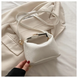 Detail of white snake-textured crossbody bag with metallic clasp on beige suit