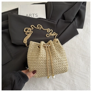 Detail of beige woven bucket bag with gold chain strap and decorative pearl drawstrings