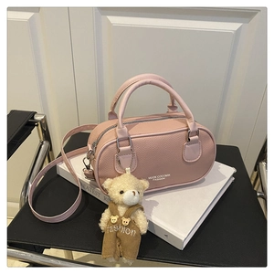 Pink barrel bag with lychee grain texture and cute plush bear charm on white books