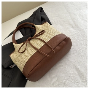 Detail of straw woven tote bag with brown leather handles and decorative bow accent