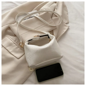 Detail of white snake skin embossed handbag with gold hardware on beige aesthetic background