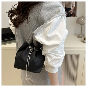 Détail du sac seau noir avec texture crocodile, chaîne en métal et accents de perles