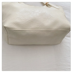 Dettaglio della base della borsa tote crema con cuciture pulite e finiture in metallo oro