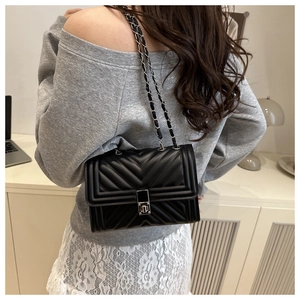 Detail of black quilted leather shoulder bag with metallic chain strap worn by a model