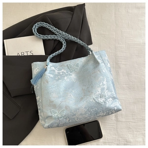 Macro detail of a light blue jacquard tote with 3D white butterfly embroidery and tassels