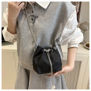 Detail of black mini bucket bag featuring butterfly metal clasp and pearl drawstring accents