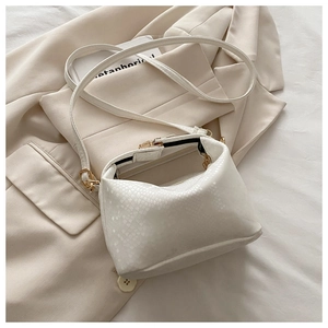 Detailed view of white crocodile embossed leather bucket bag with metallic clasp closure