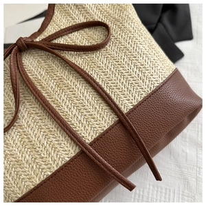 Detail of woven straw handbag with brown faux leather trim and decorative bow accent