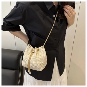 Detail of woven straw bucket bag featuring a gold chain drawstring and pearl charms