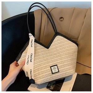 Detail of woven straw tote bag with black leather straps and decorative logo ribbon