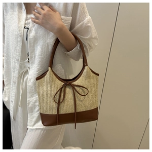 Detail of woven straw tote bag with brown leather trim and decorative bow accent