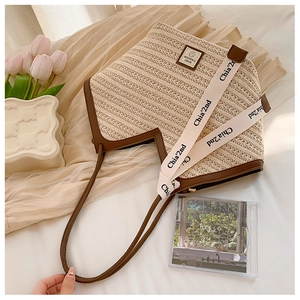 Detail of woven beach tote with leather trim and wide logo strap on neutral background