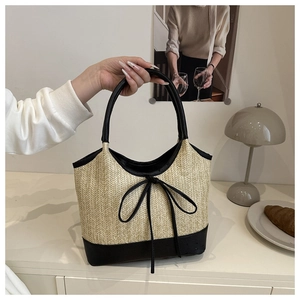 Detail of woven straw tote bag featuring black leather trim and minimalist bow decoration