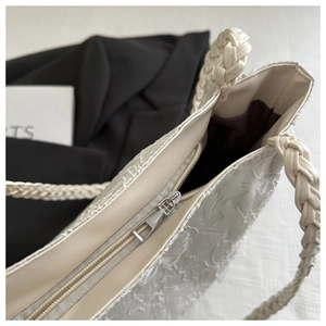 Detail of cream tote bag featuring lace embroidery, woven handle and silver zipper closure