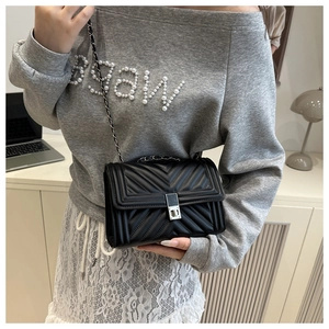 Detail of black V-quilted chain bag with silver twist lock and leather strap