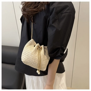 Detail of woven straw bucket bag featuring gold chain strap and elegant pearl charms