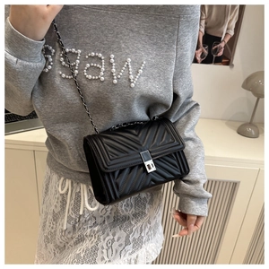 Close-up of black quilted crossbody bag with silver twist lock and chain strap on model