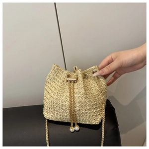 Close-up of woven straw bucket bag with gold chain strap and elegant pearl drawstring