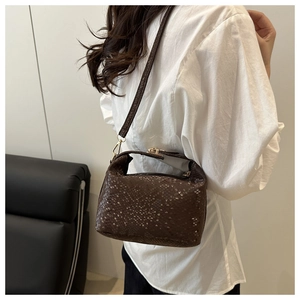 Detail of dark brown snakeskin pattern handbag with metal buckle worn by a model