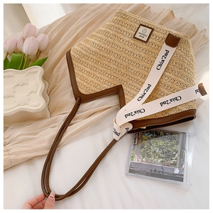 Close-up of a straw tote bag with brown leather trim and wide canvas shoulder strap