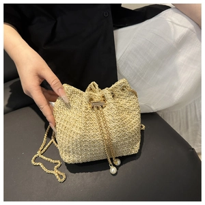 Detail of woven straw bucket bag featuring gold chain strap and pearl drawstring tassels