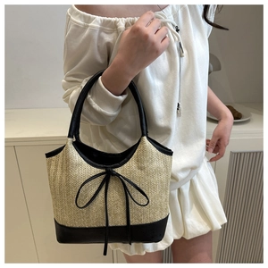 Close-up of woven straw tote bag with black leather handles and bow detail