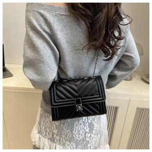 Detail of a black quilted leather crossbody bag with metal chain strap worn by a model